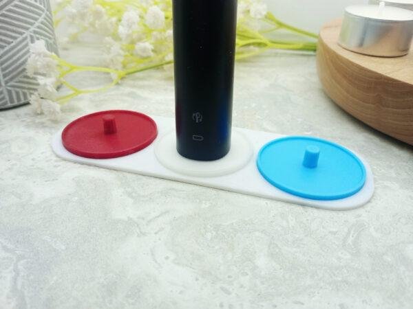 The image shows a 3 person toothbrush holder with an Philips Sonicare toothbrush placed on the central holder. The toothbrush gives a sense of scale and shows that three toothbrushes could fit comfortably while not taking up too much room. Three person electric toothbrush holders. Available in different colours. Choose from green, blue, yellow, red and white. Choose your own colours.