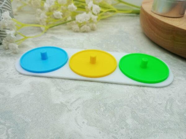 A 3 person electric toothbrush holder is displayed from a corner perspective. It has three different colour holders on a white base. Each holder is suitable for a Philips Sonicare toothbrush. The slender base piece elegantly joins the three coloured piece together. Three person electric toothbrush stand. Available in different colours. Choose from green, blue, yellow, red and white.