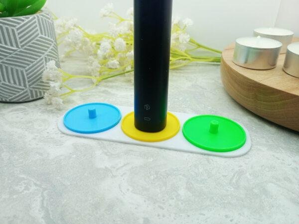 This image is of a 3 person electric toothbrush holders compatible with Philips Sonicare toothbrushes. It is an photo taken from above with a background of a dark marble effect tile. It shows clearly the curved corners of the base piece that joins the three holders together and the circular nature of the holders. Three person electric toothbrush holders. Available in different colours. Choose from green, blue, yellow, red and white. Displays blue, yellow and green.