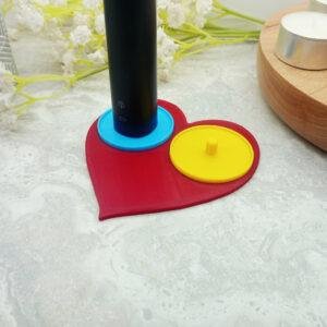 A romantic heart shaped toothbrush holder suitable for Philips toothbrushes. The image shows the red heart of the holder base with two bright circular holders of yellow and blue mounted on top. The two person heart shaped electric toothbrush holder is a modern, playful romantic gift for couples moving in together or as a fun romantic 'his and her' gift.