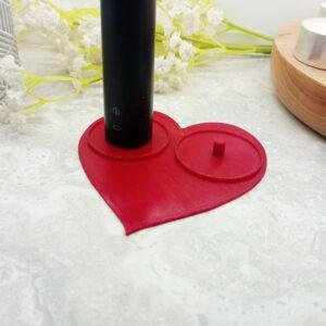 Red, heart shaped Philips electric toothbrush holder shown from above. This shows clearly the classic heart shaped with clean modern lines. There are standard size tealights included in the image to give a sense of scale. the circular lips surrounding the toothbrush mounts can be seen.