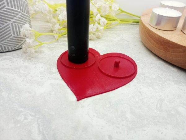 Red, heart shaped Philips electric toothbrush holder shown from above. This shows clearly the classic heart shaped with clean modern lines. There are standard size tealights included in the image to give a sense of scale. the circular lips surrounding the toothbrush mounts can be seen.