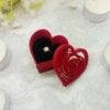 The red heart shaped ring gift box is surrounded with tealights to give a sense of scale. The lid for the box is leaning against the box so you can see the depth of the lid and the box. The red of the box is contrasted by the black of the ring display foam that holds the ring upright. The ring fits nicely into the box, leaving enough room not to be cramped but enough room to show the ring to its best advantage. The ring is not included.